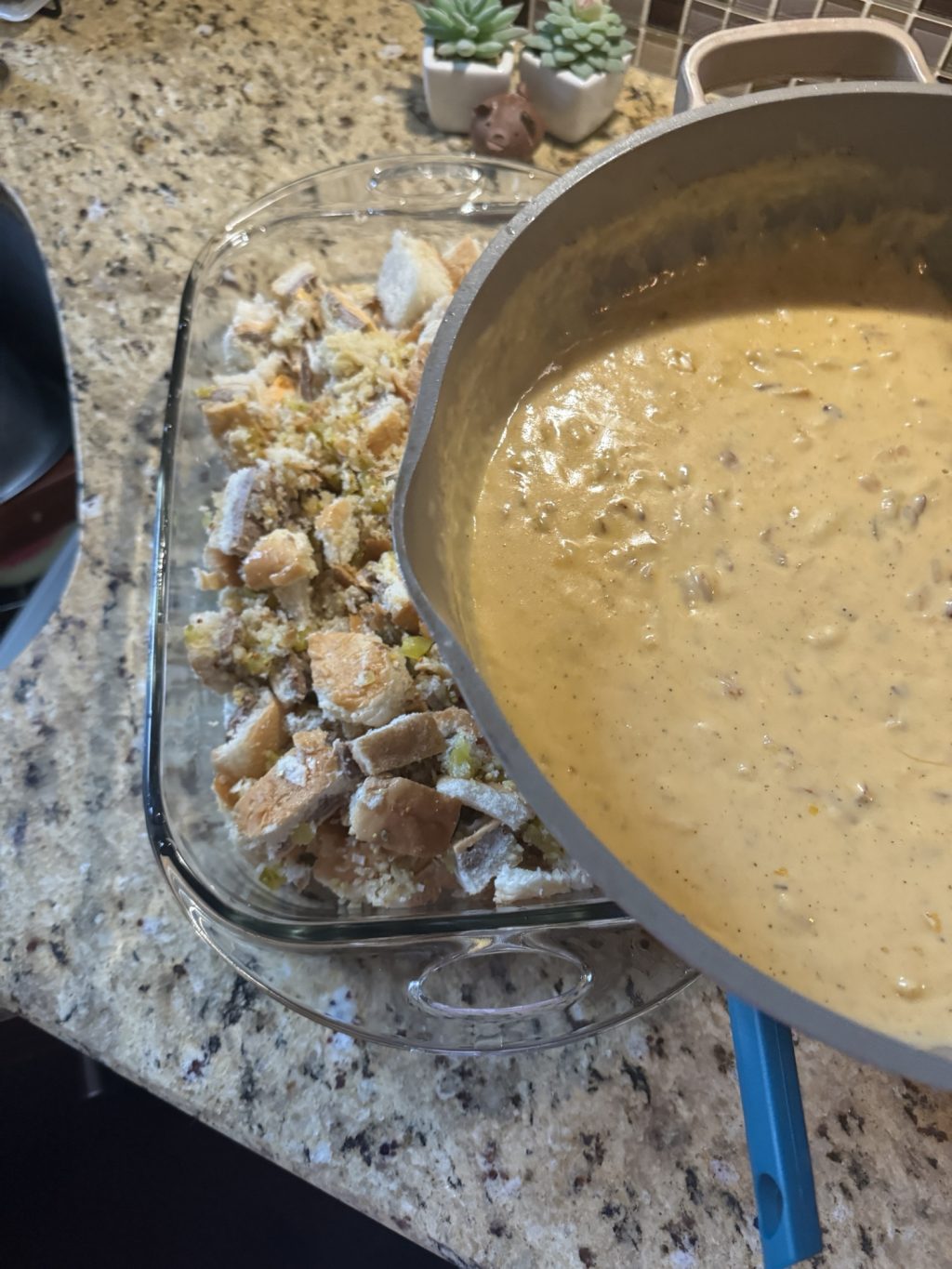 Cheese sauce about to be poured from a pan on to a glass baking dish of chopped sliders