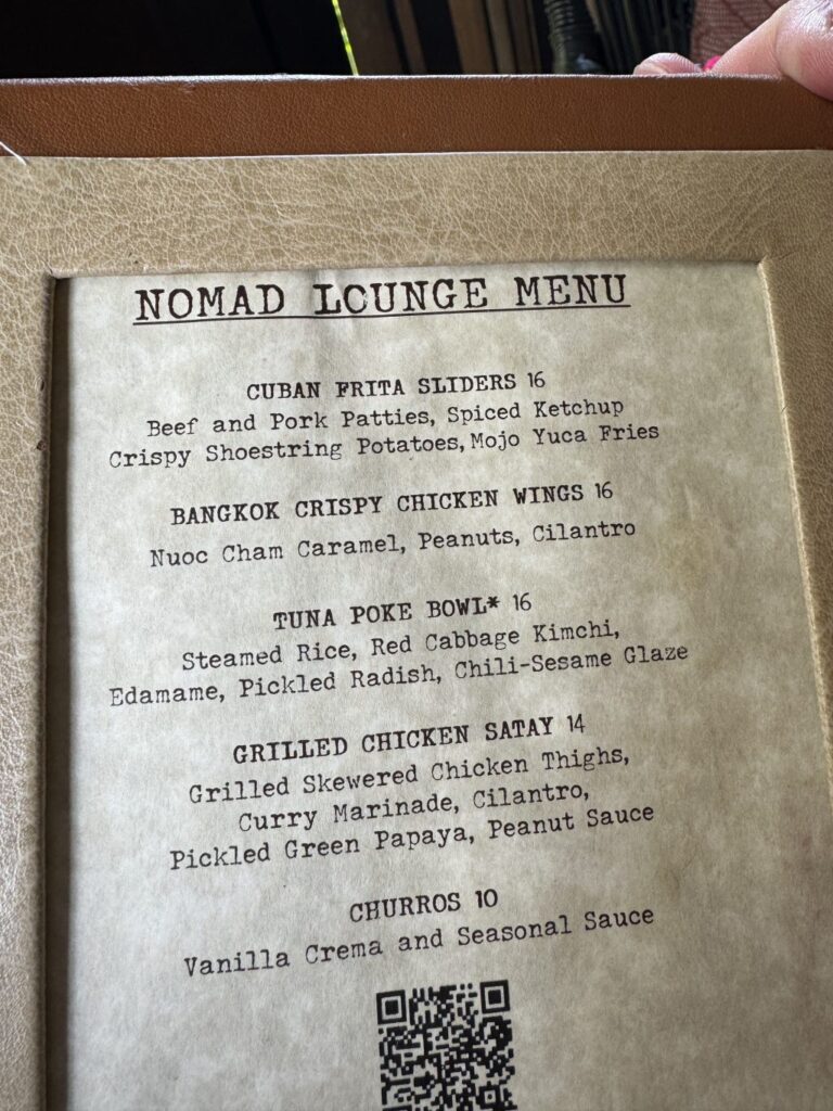The Nomad Lounge Menu featuring dishes like Cuban Frita Sliders, Bangkok Crispy Chicken Wings, Tuna Poke Bowl, Grilled Chicken Satay, and Churros