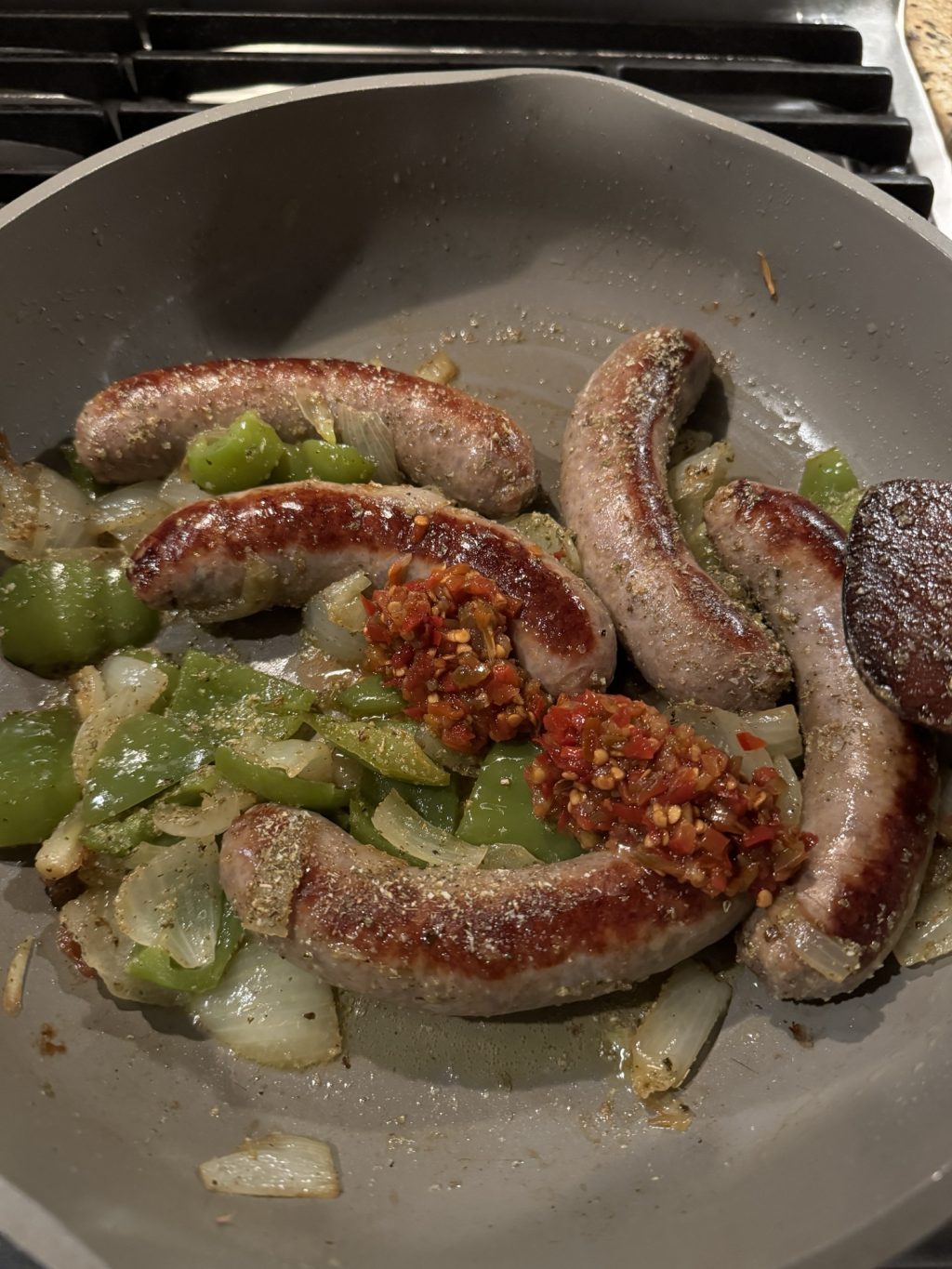 Sausages, peppers, and cherry pepper spread cooking in a pan
