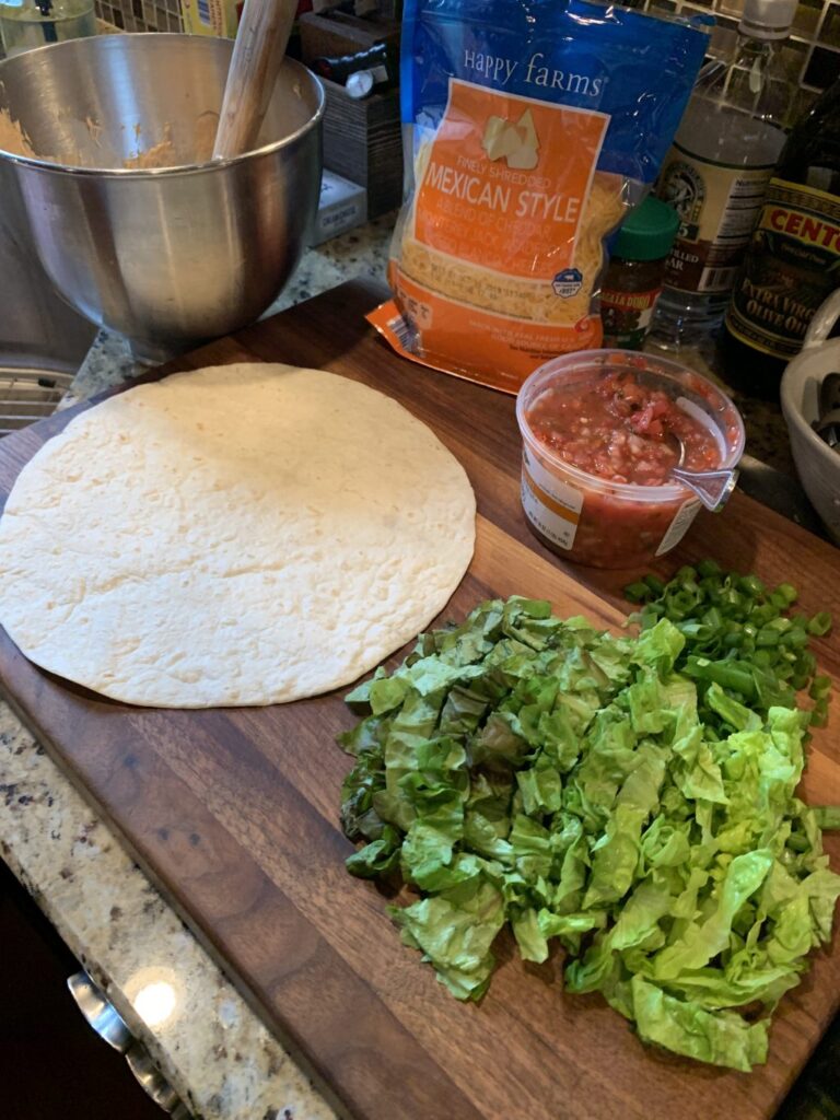 A flour tortilla on a cutting board with shredded lettuce and salsa