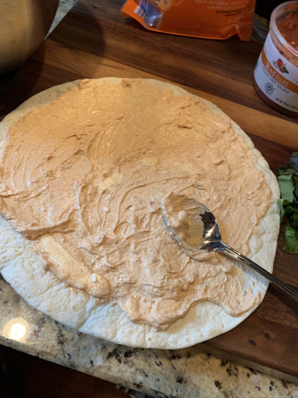 Cream cheese mix being spread on a tortilla with a spoon
