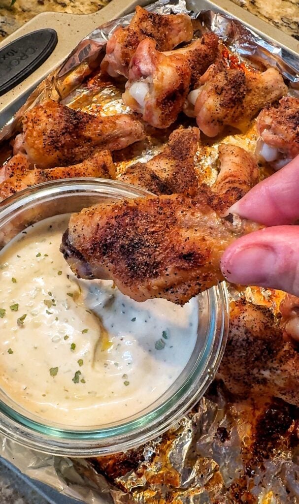 A crispy wing being dipped into white sauce