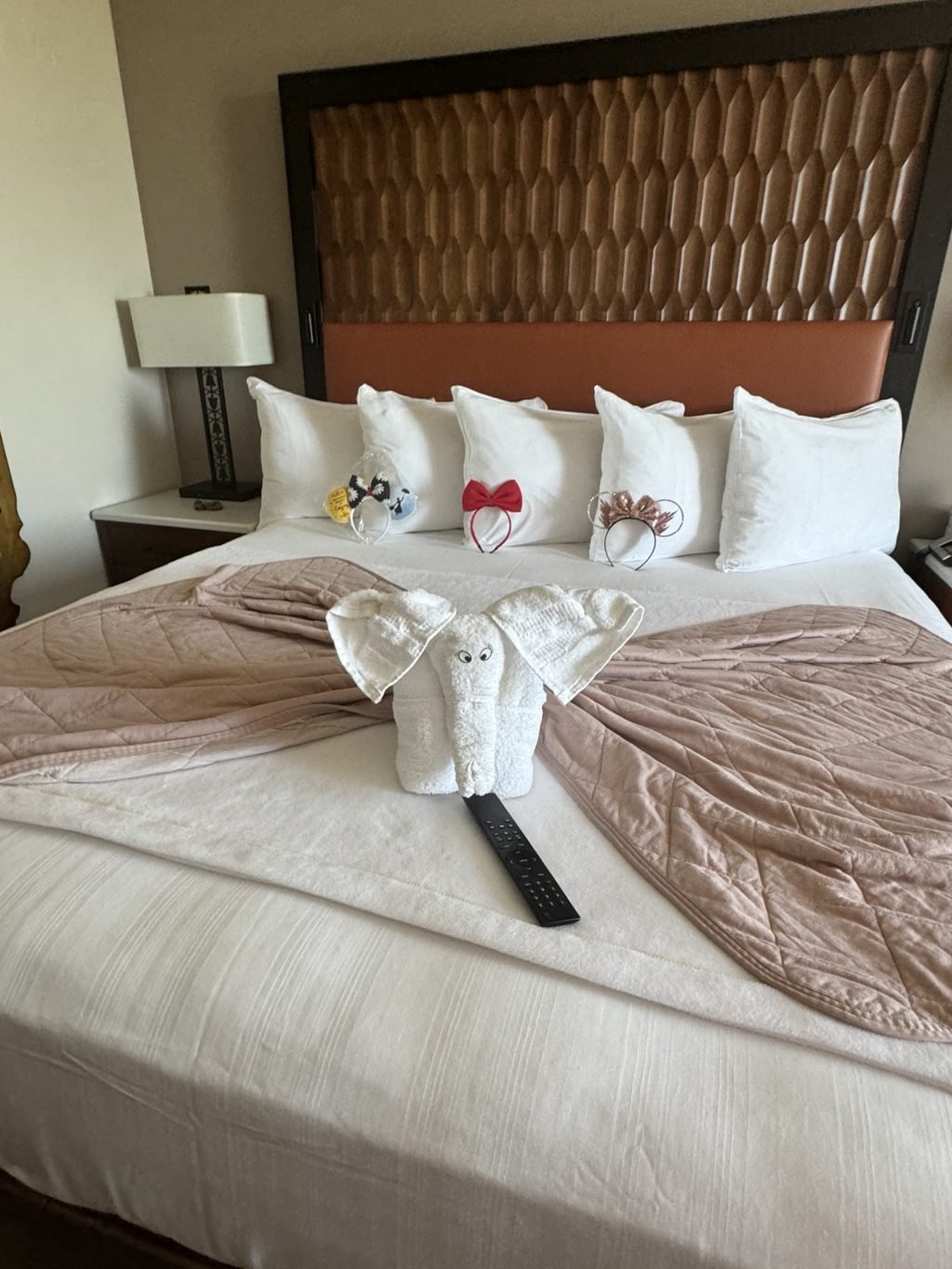 The bed at Coronado with a towel elephant and remote control on it and three headbands stood up against the pillows