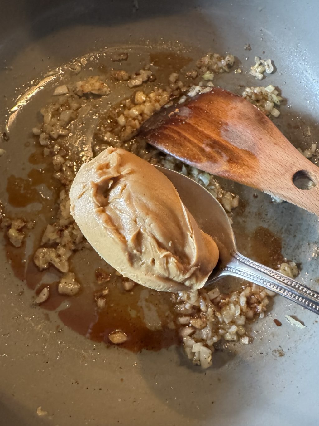 A spoon of peanut butter over sizzling onions.