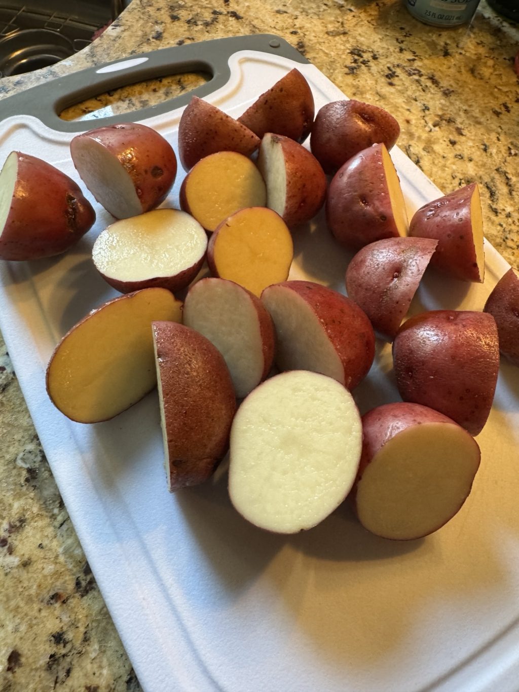 Raw, baby red potatoes cut in half on a white cutting board