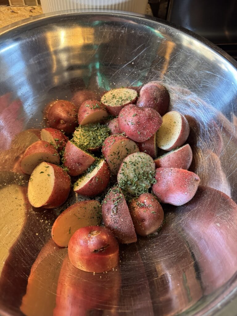 Halved baby red potatoes in a metal bowl covered in seasonings
