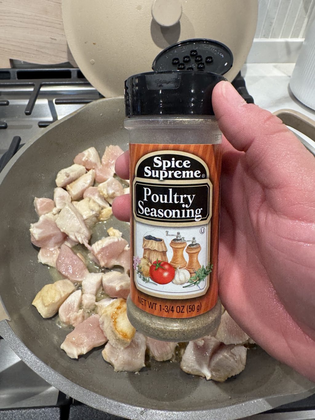 A shaker of poultry seasoning over a pan of cooking chicken pieces