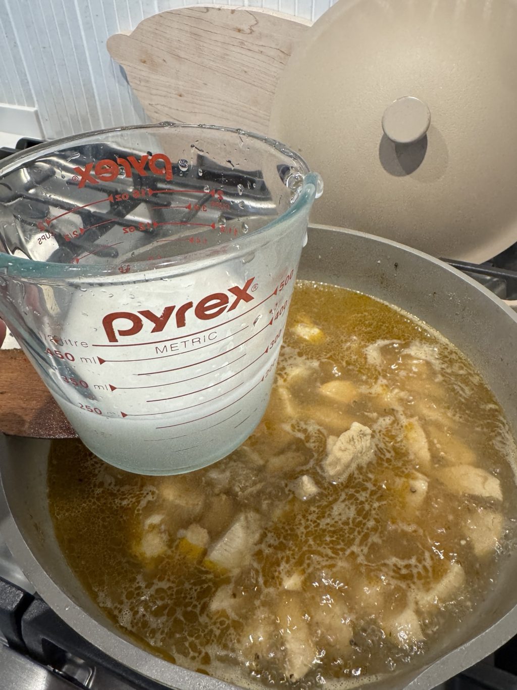 Corn starch in a Pyrex over chicken simmering in a pan