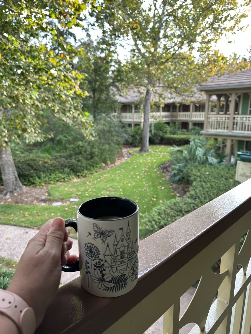 A coffee mug held on a railing overlooking the ground of the Port Orleans Resort