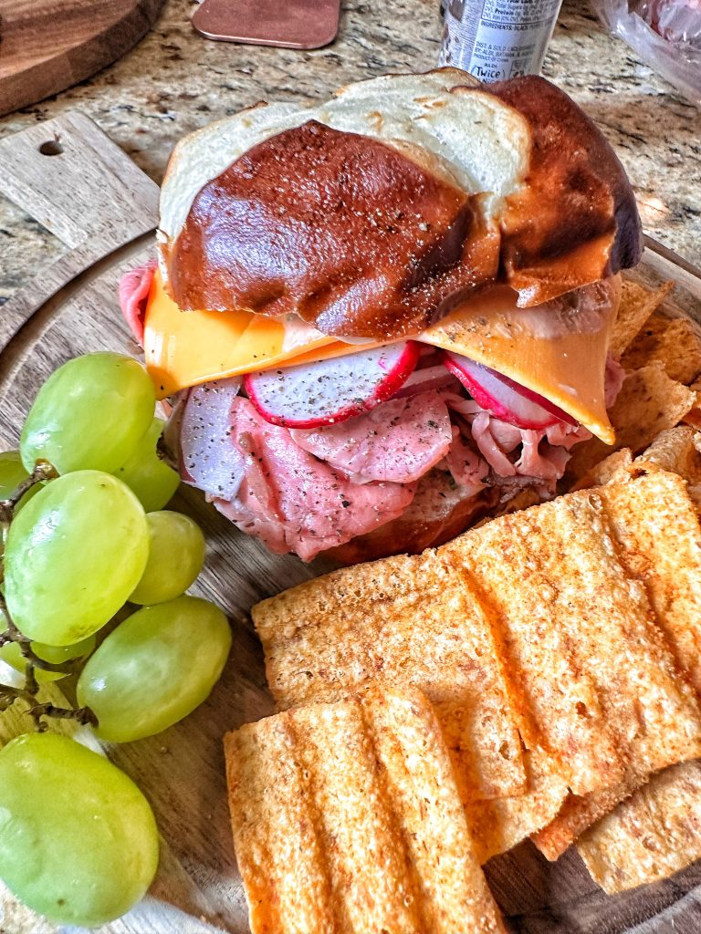 A roast beef sandwich with grapes and Doritos