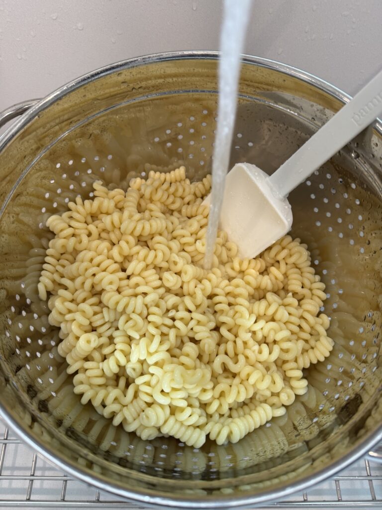 Fusilli pasta being rinsed in a strainer