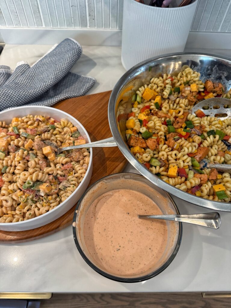The finished pasta salad in two big bowls next to a bowl of dressing