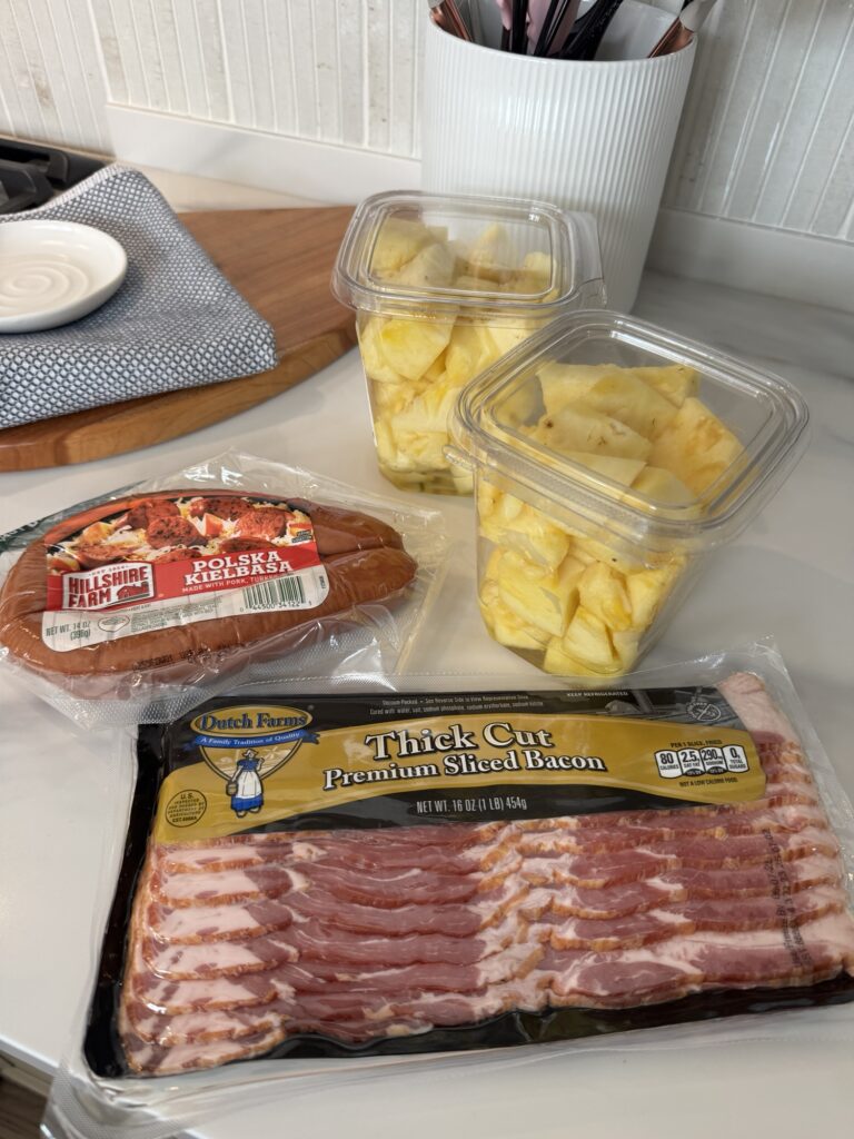 Two containers of sliced pineapple, a package of Polish Kielbasa, and a package of thick cut bacon