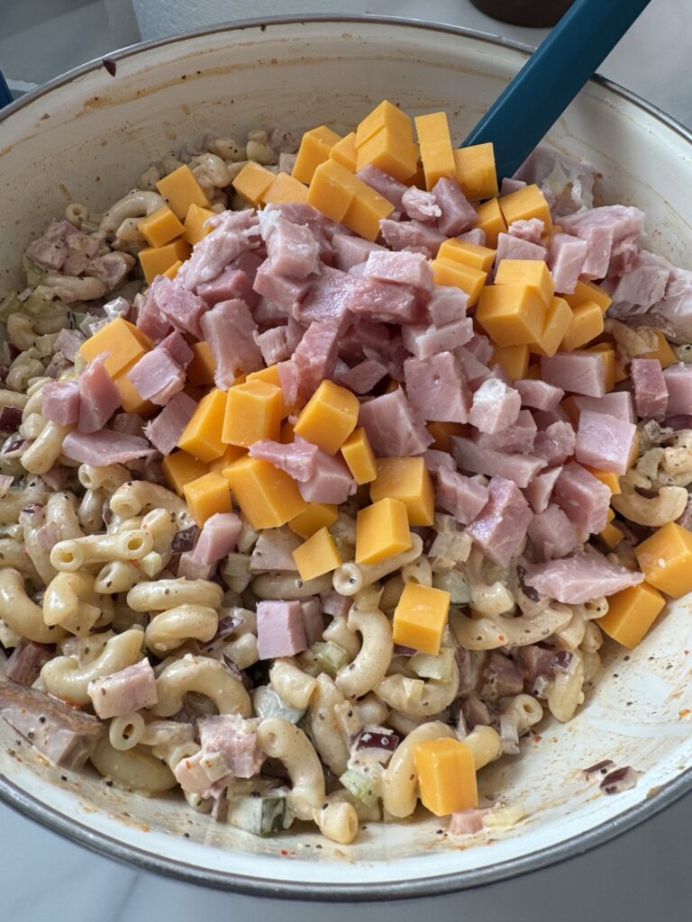Diced ham and cheese being mixed into macaroni salad