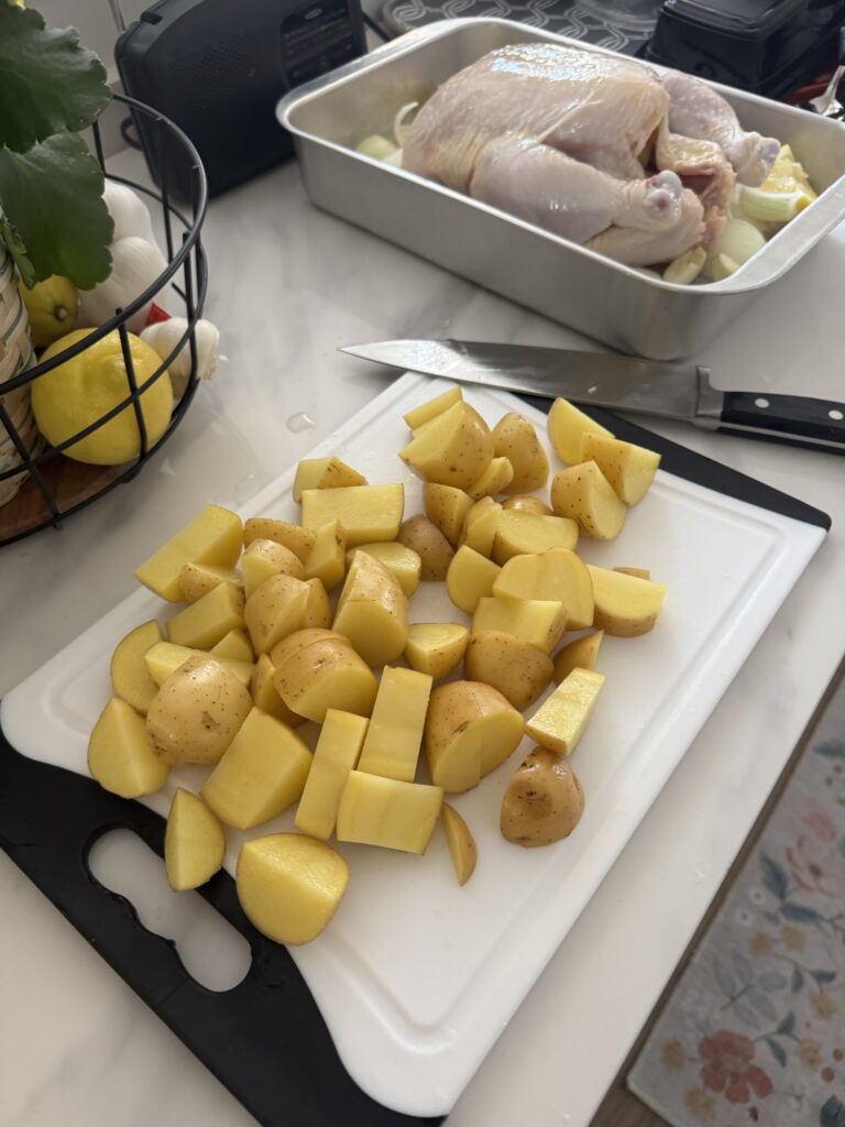 Chopped potatoes on a cutting board in front of raw chicken in a baking dish