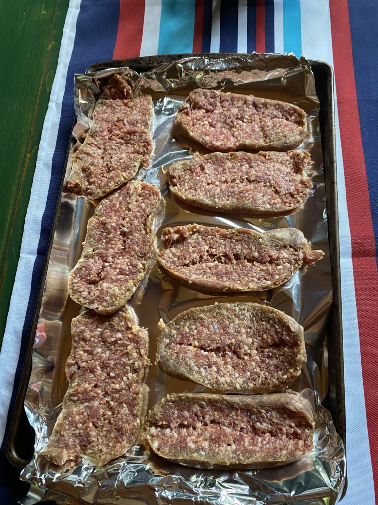 Split, uncooked sausages on a foil baking sheet