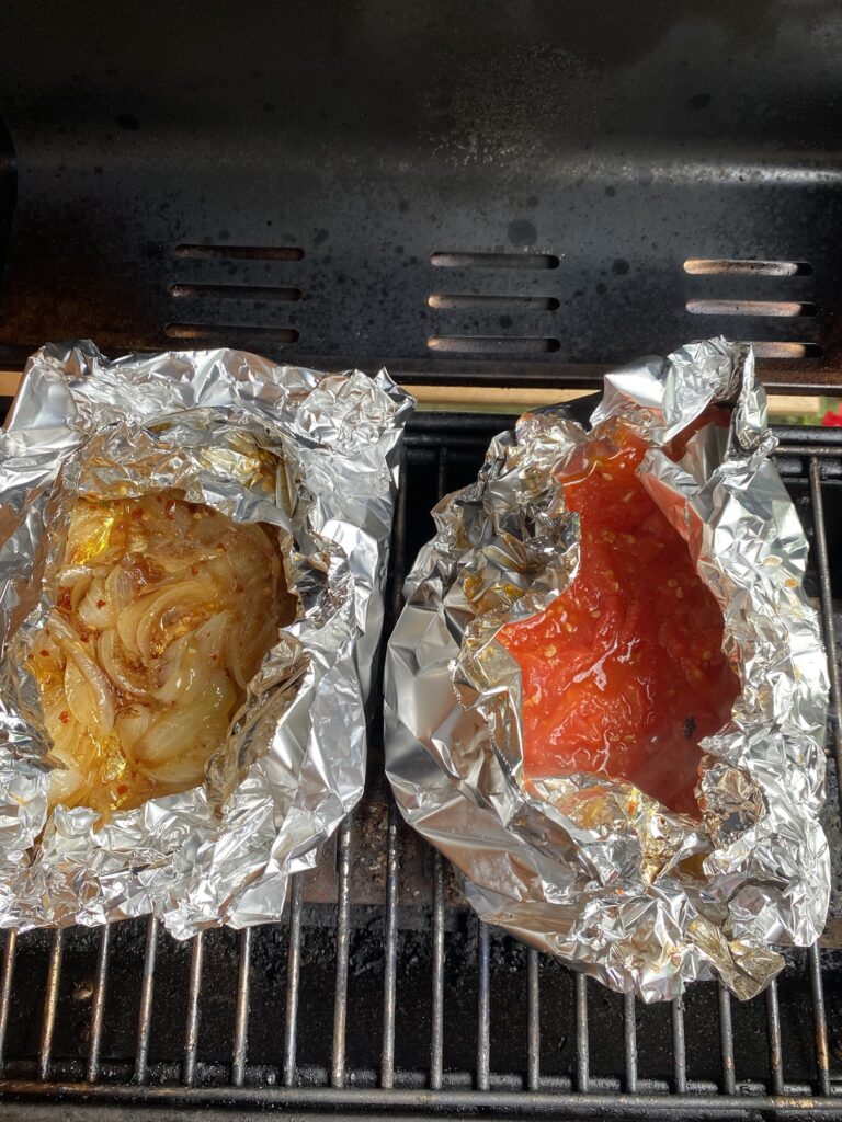 Foil packets with onions and tomato sauce, respectively, on the grill