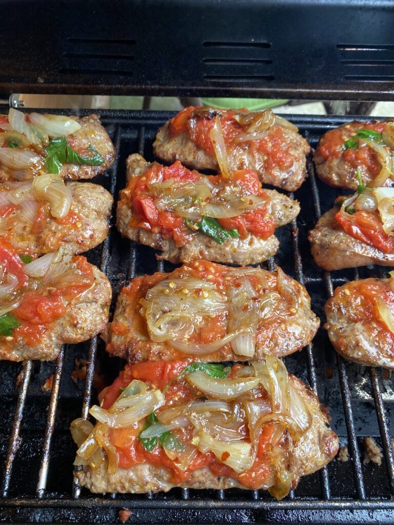 Tomato sauce and onions on top of sausages cooking on the grilll