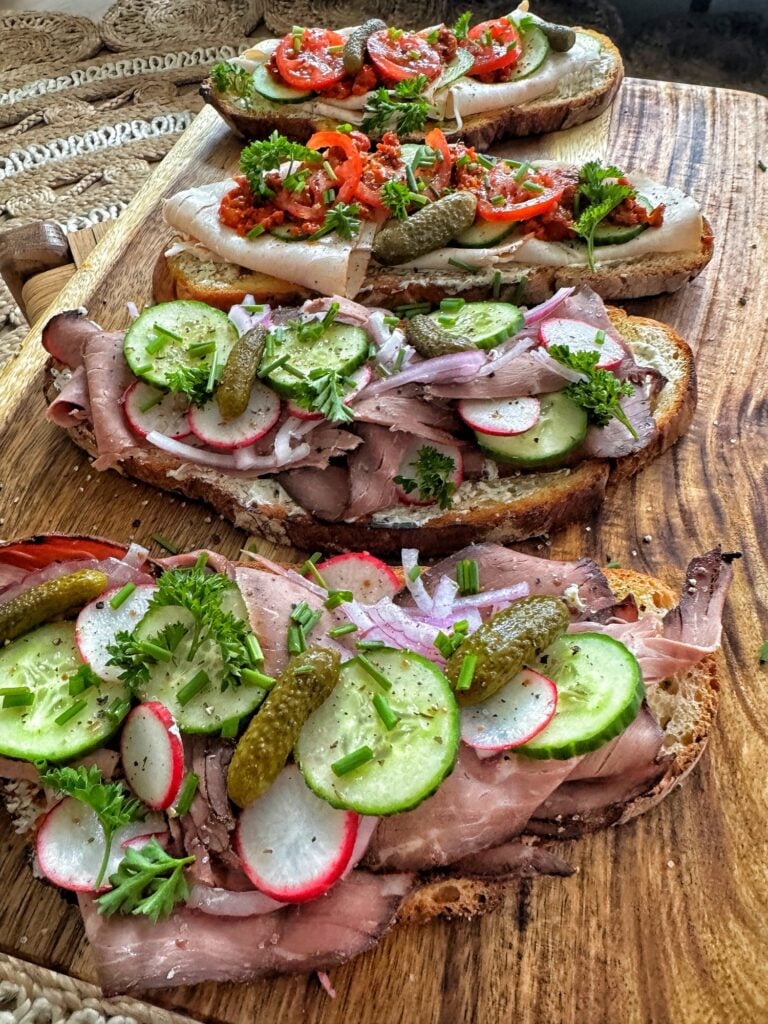 Open faced sandwiches covered in deli meat, radish, tomato, cucumbers, and garnish