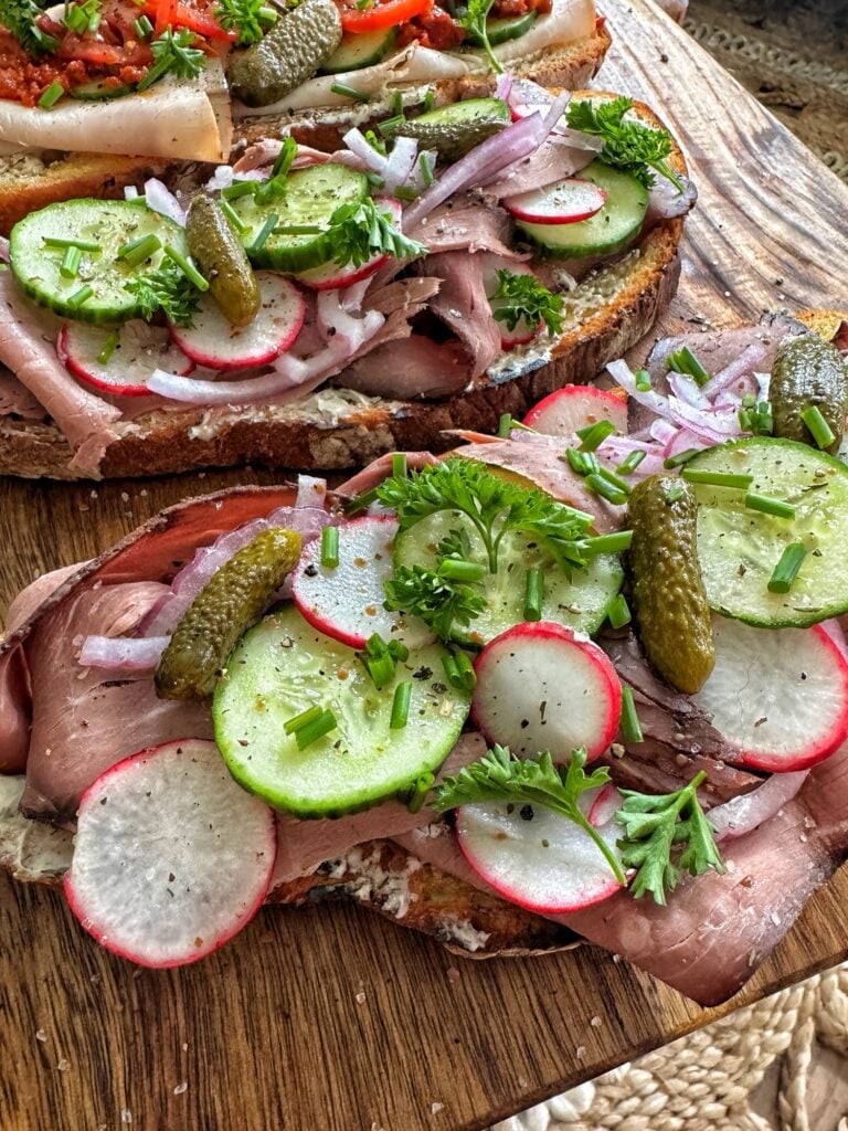 Open faced sandwiches covered in deli meat, radish, tomato, cucumbers, and garnish