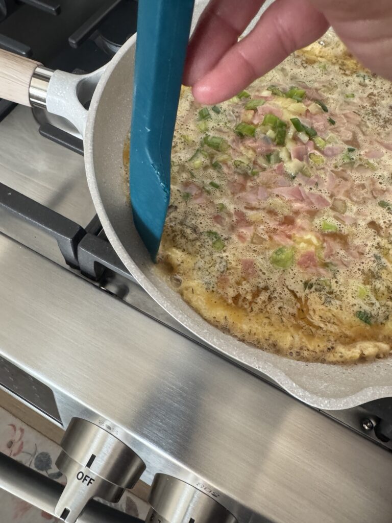 A spatula being used to scrape the omelette from the sides of the pan 
