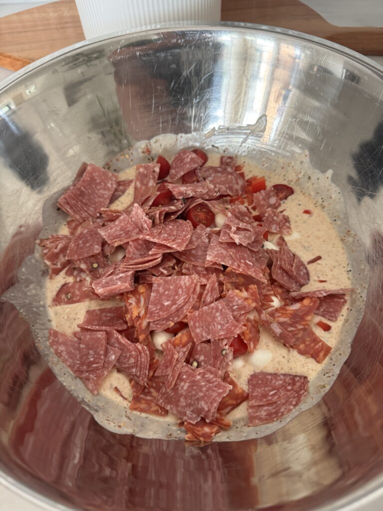 Slices of cured meats in the dressing in the metal bowl
