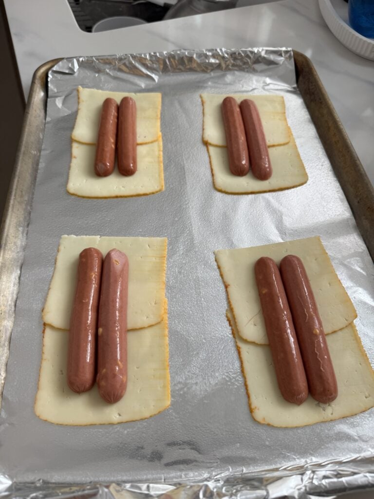 Sliced dogs placed face down on cheese on a baking sheet